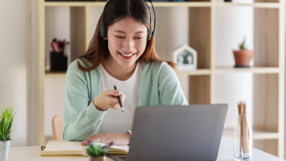 A student in an online class with a headset on sits in front of a laptop and holds a pencil.