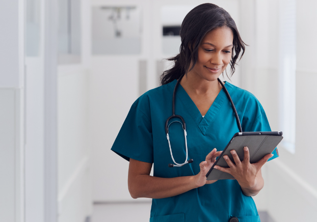 Female healthcare professional in scrubs with a stethoscope working on a tablet.
