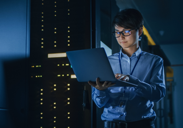 Male technology professional working on a laptop while standing in a computer software room.